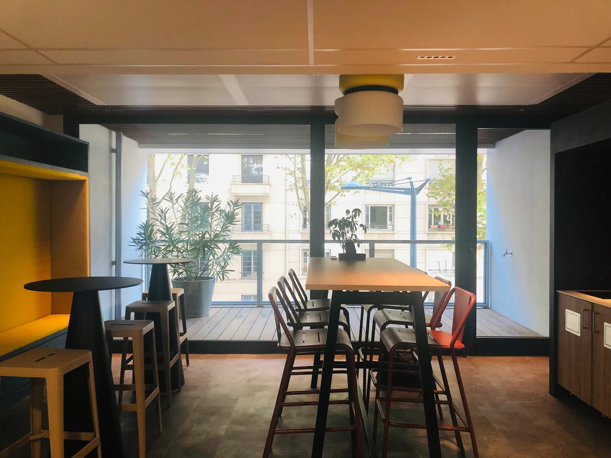 Espace commun de bureaux avec grande table, assises hautes et baies vitrées